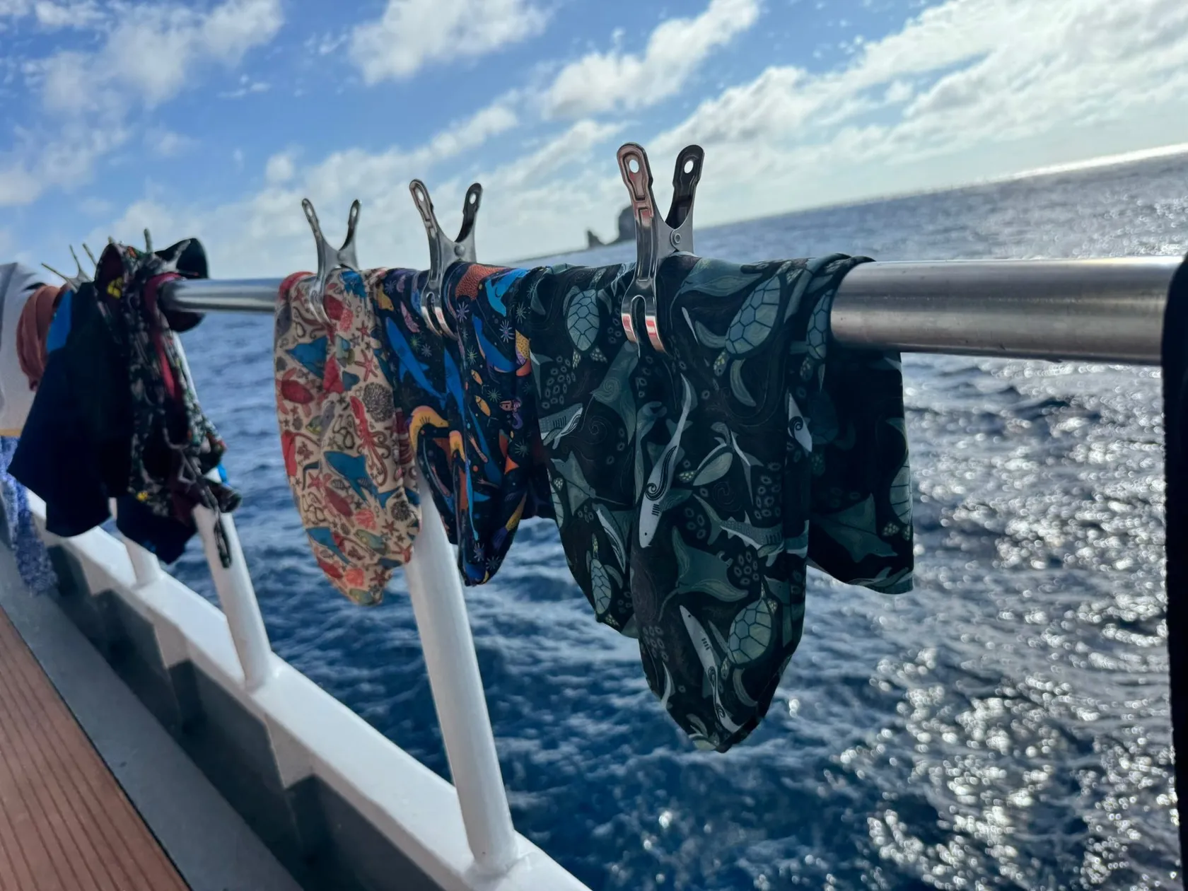 Three hand-sewn dive sock prototypes drying on a boat railing, Kicker Rock on the horizon