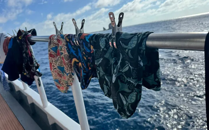 Three hand-sewn dive sock prototypes drying on a boat railing, Kicker Rock on the horizon