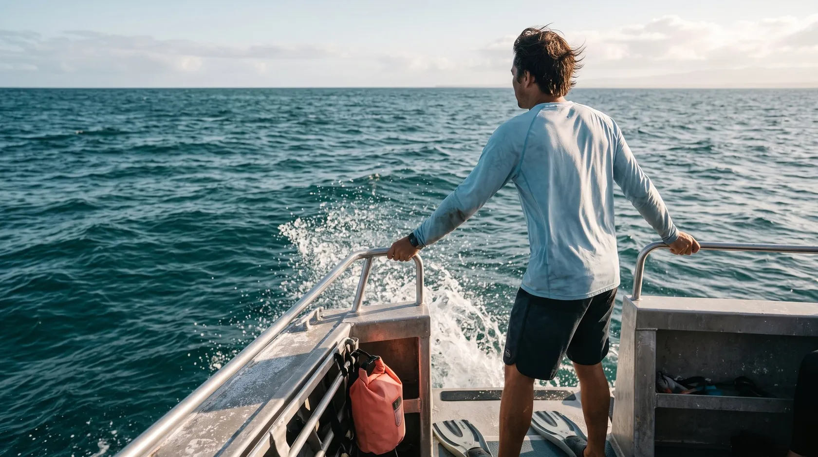 Person at the stern of a dive boat holding the railing and watching the horizon