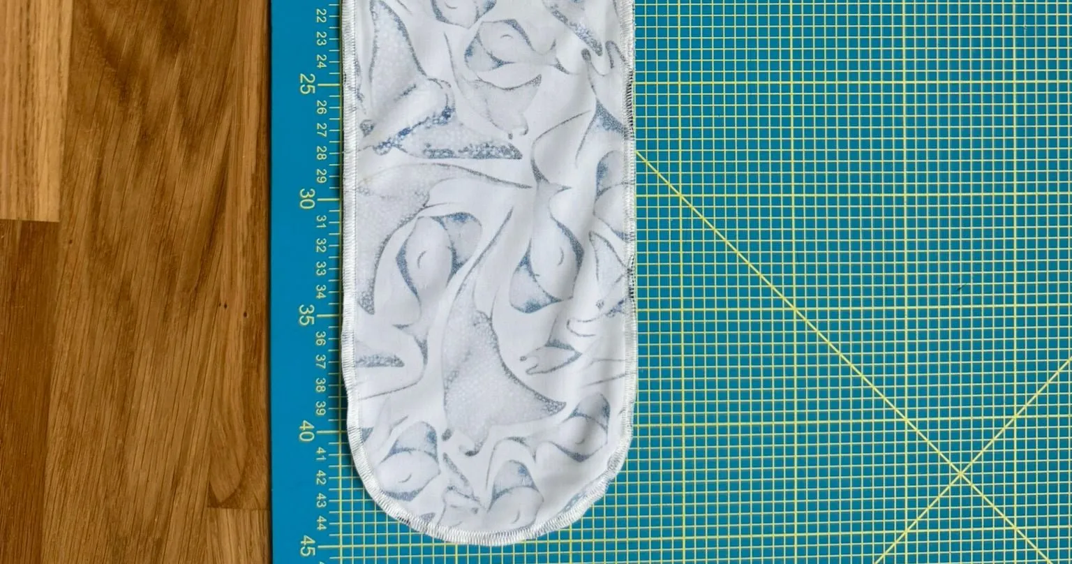 An early dive sock prototype lying inside out on a cutting mat next to a ruler